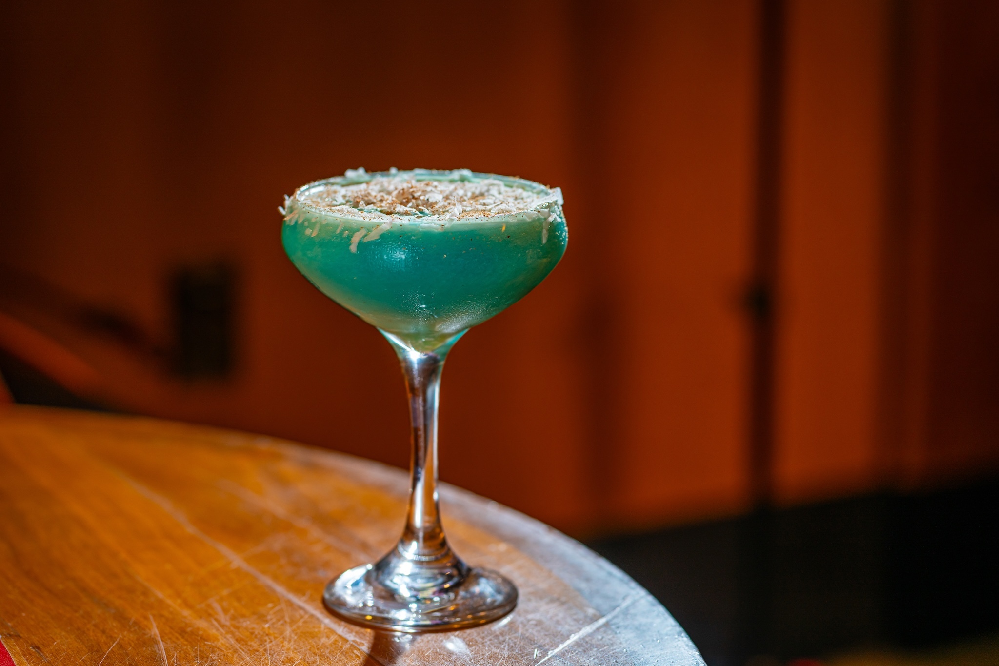 A blue cocktail in a coupe glass with coconut on the rim