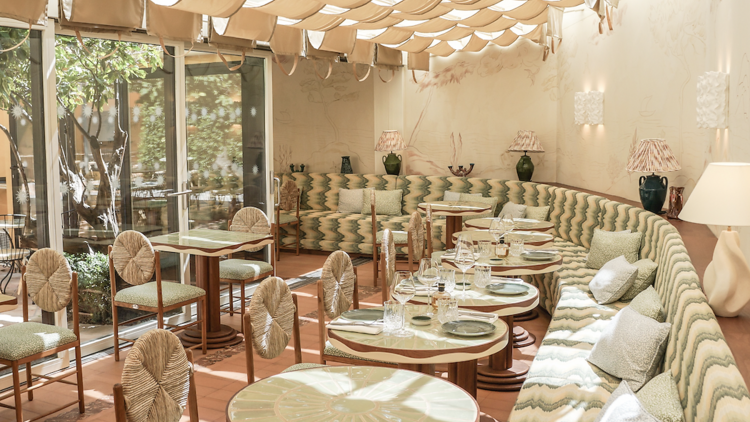 Interior of restaurant with a long booth along the back wall accompanied by  small dining tables. 