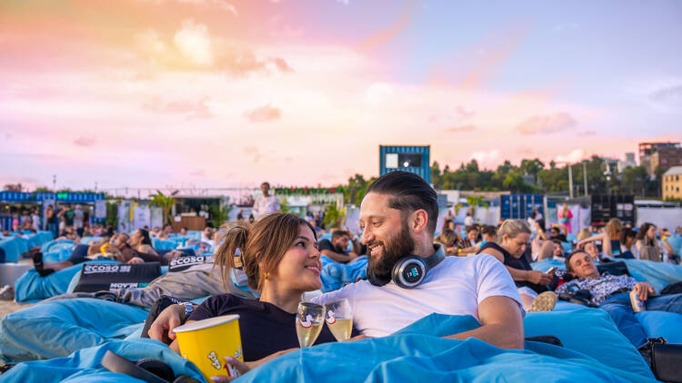 A couple sitting on a bed at an outdoor cinema.