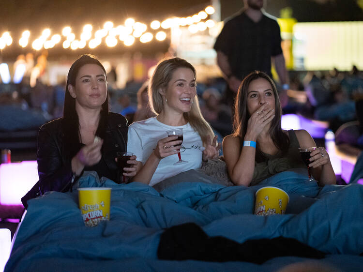 Three people sitting together eating popcorn watching a movie. 