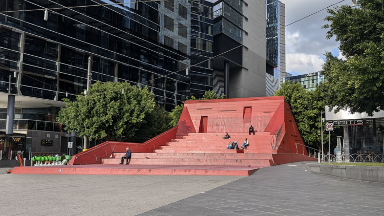 A huge red staircase with a few people sitting on it. 