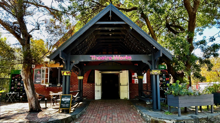 The outside of the timber theatre works building with a triangular porch and a red brick entry path