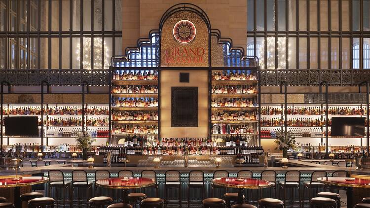 Head on picture of Grand Brasserie restaurant with wrought iron bars, a bar and a clock on the wall