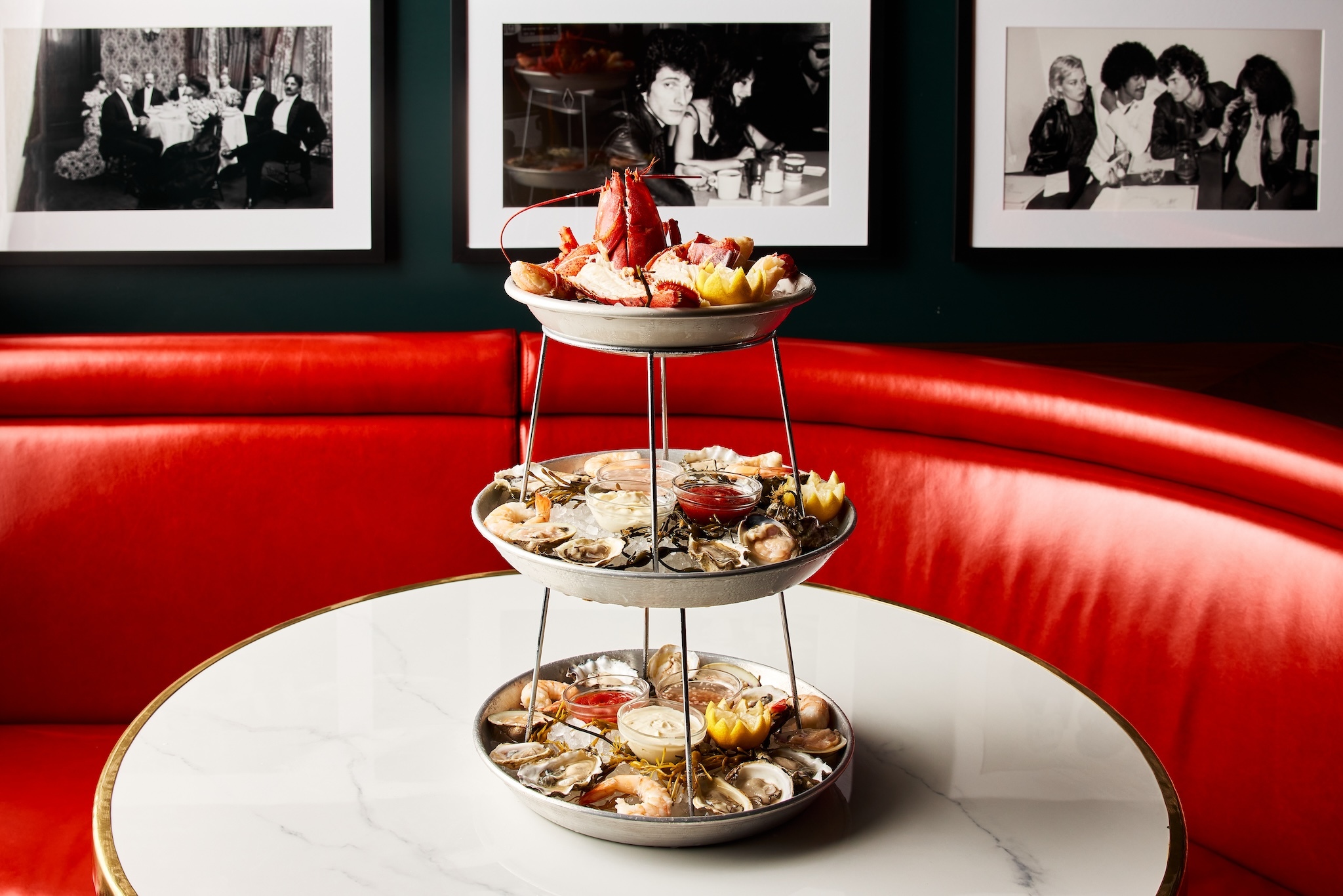 A three-tiered seafood tower sitting on a white table with a red booth in the background