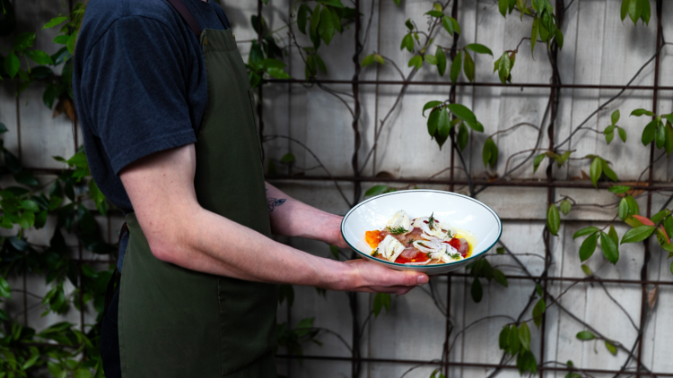 Chef carrying a dish in the courtyard.