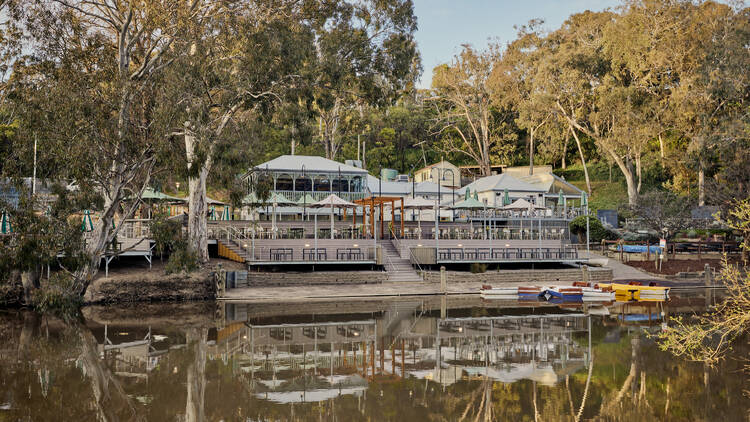 A large building on the bank of a river, surrounded by trees. 