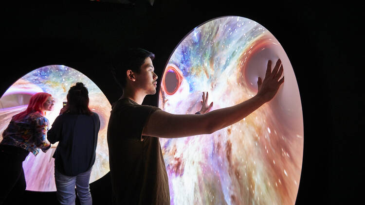 People touching circular screens showing projections of outer space, in the Beyond Perception exhibition at Scienceworks