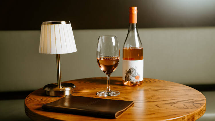 A bottle and glass of rosé on a wooden table.