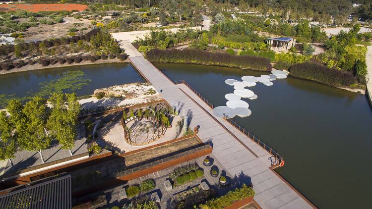 An aerial view of a garden with a lake and a footbridge. 