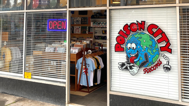 The front window of Poison City Records showing a logo of a world holding a record.