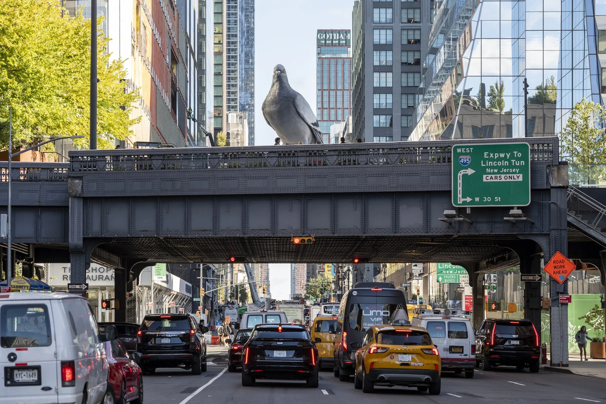 A sculpture of a pigeon on a bridge over NYC traffic.