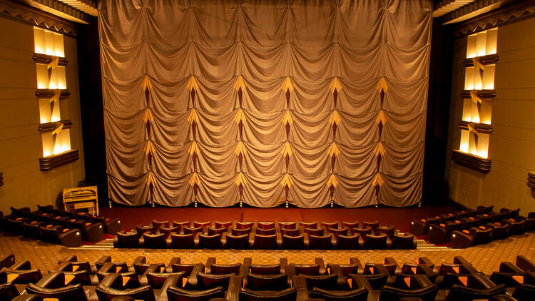 The interior of a cinema with leather chairs and a draping curtain. 