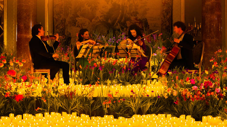 A string quartet surroundd by candles and flowers.