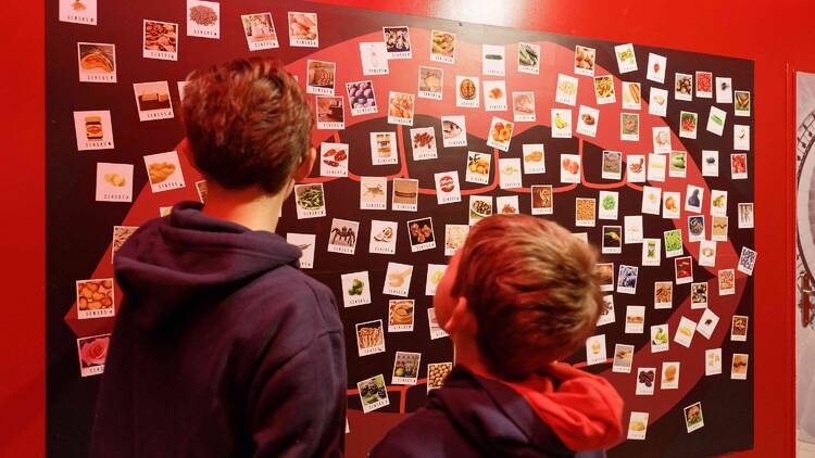 People looking at a wall filled with photos of food. 