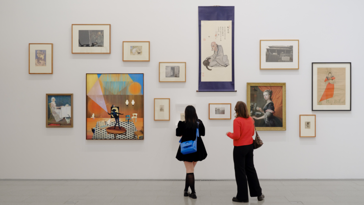 Two women looking at artworks featuring cats