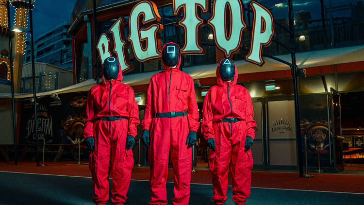 People in red suits with masks on, in front of the words BIG TOP