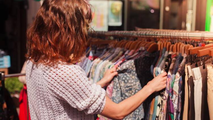 A woman browses a rack of clothes at a street market.