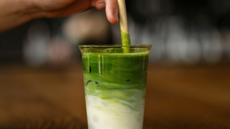 Matcha a hand holding a wooden stick over a green drink