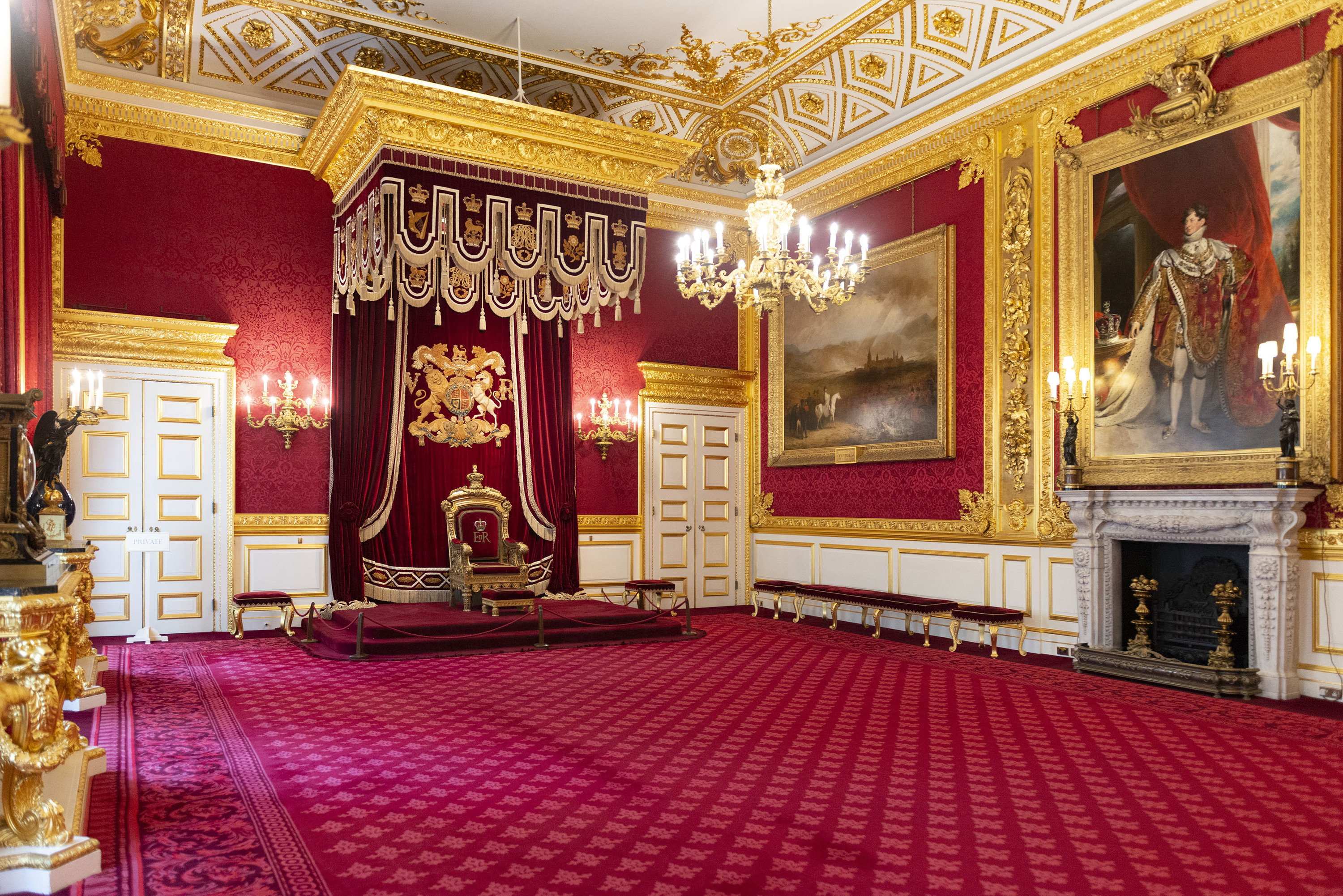 The Throne Room at St James’s Palace with a red and gold throne, red carpet and gold-framed paintings.