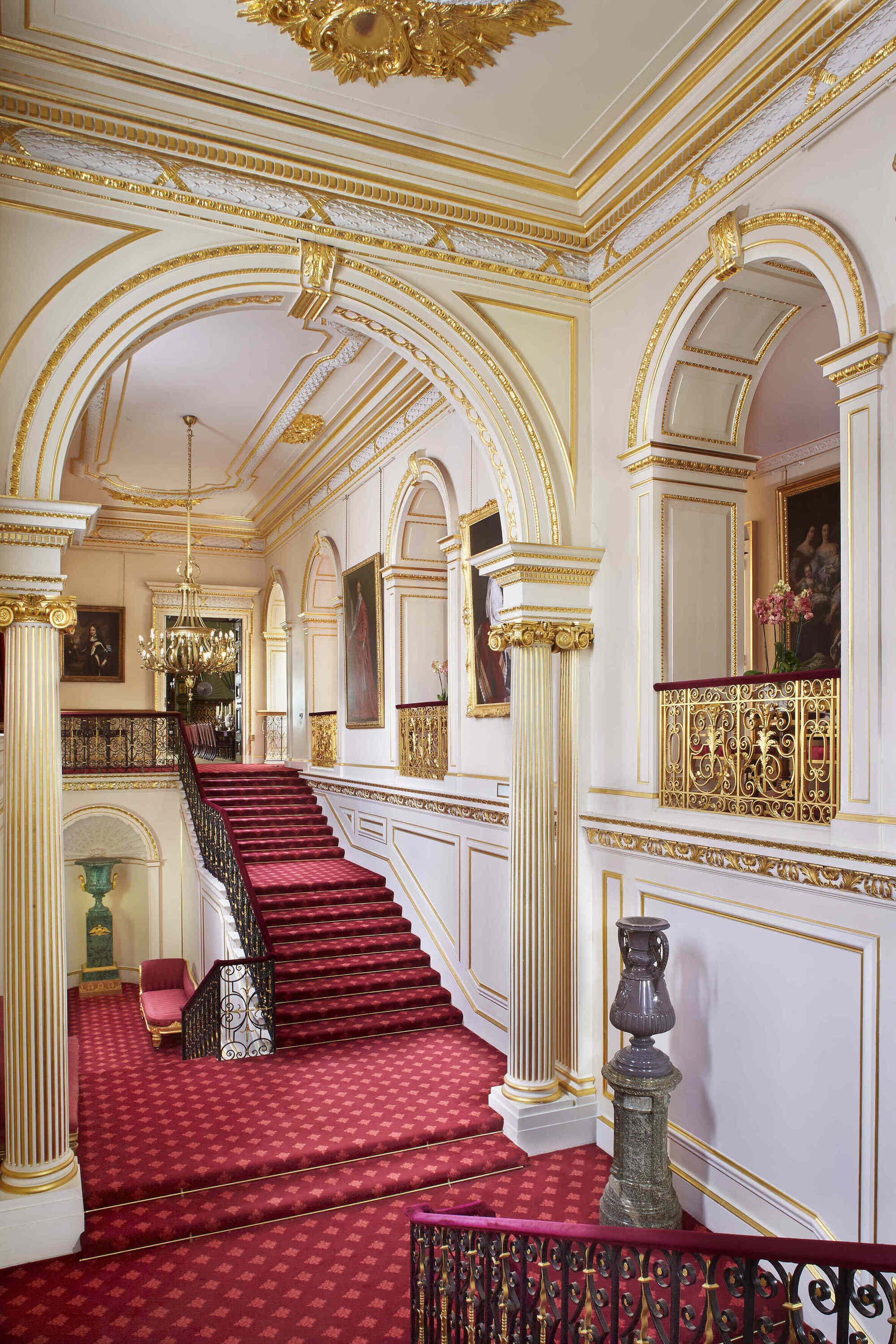 The Grand Staircase at St James’s Palace, with white and gold columns and red carpet. 