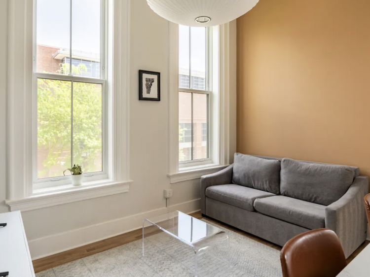 Living room with large windows, a sofa, rug and clear coffee table.