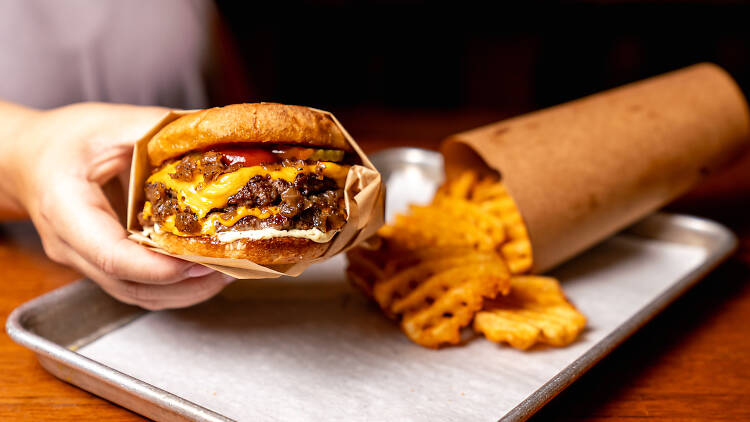 A person hold a burger with waffle fries in the background