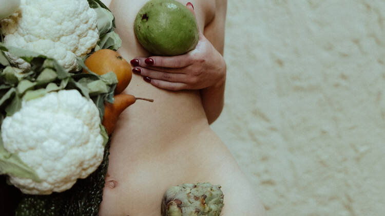 A naked torso posing with vegetables like cauliflower and artichokes.