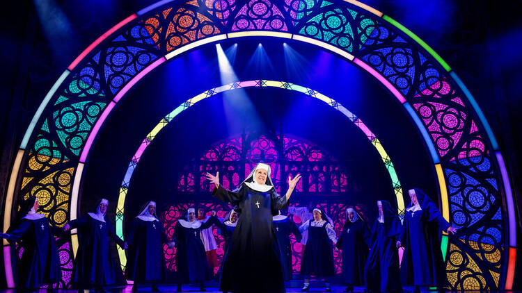 Rhonda Burchmore on stage in Sister Act with the cast behind her.