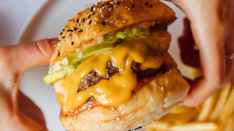 A person holding a burger over a plate of fries