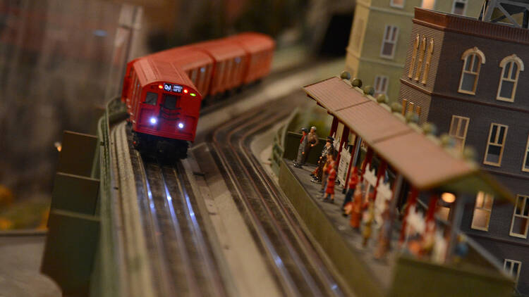 A red train chugs along a track on a model railroad.