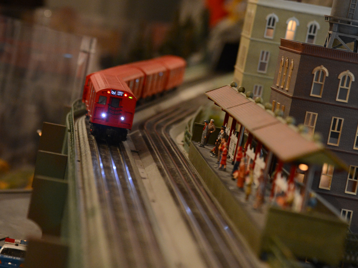 A red train chugs along a track on a model railroad.