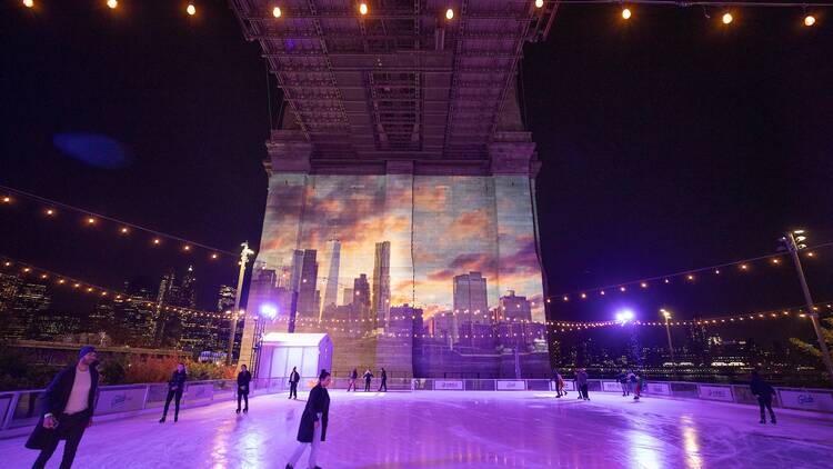 Skaters glide along an ice rink under the Brooklyn Bridge.