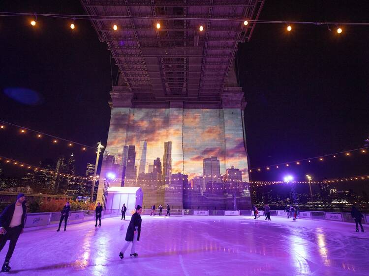 Skaters glide along an ice rink under the Brooklyn Bridge.