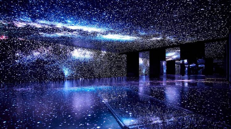 Lit-up stars fill the ceiling, walls, and floor in a darkened room at an immersive exhibit.