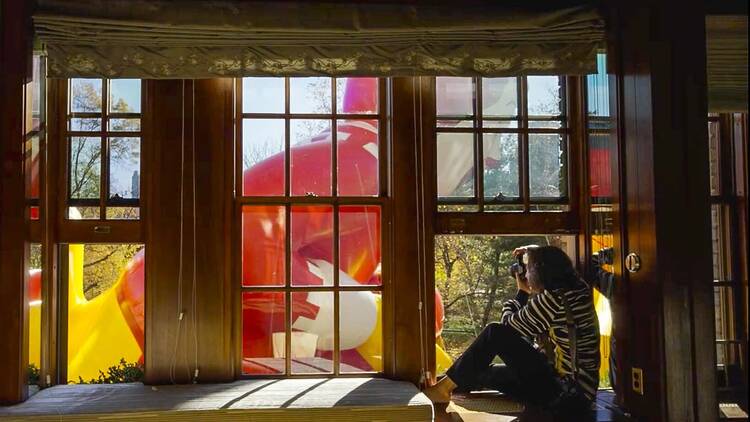 A woman sits in her window taking photos of a Macy's Thanksgiving Day Parade balloon of Ronald McDonald.