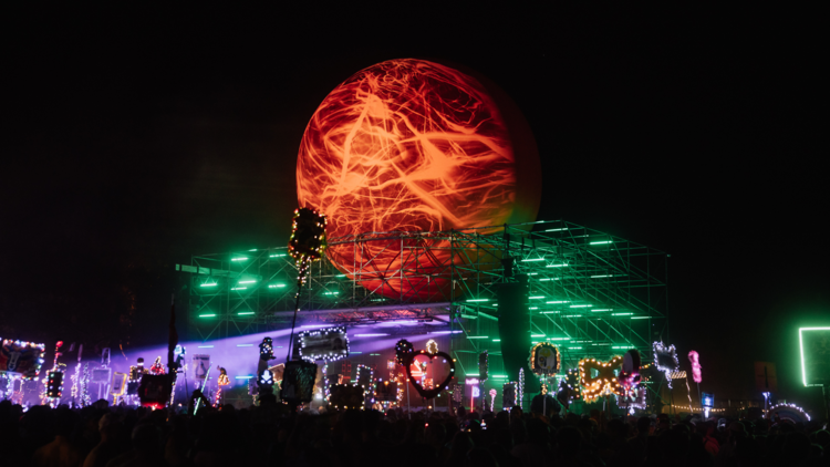 An illuminated stage with a crowd of doof sticks and a large red sphere above