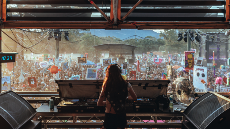 A dj with long hair plays to a large crowd in the daytime