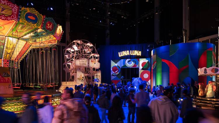 People gather inside Luna Luna looking at amusement park rides.