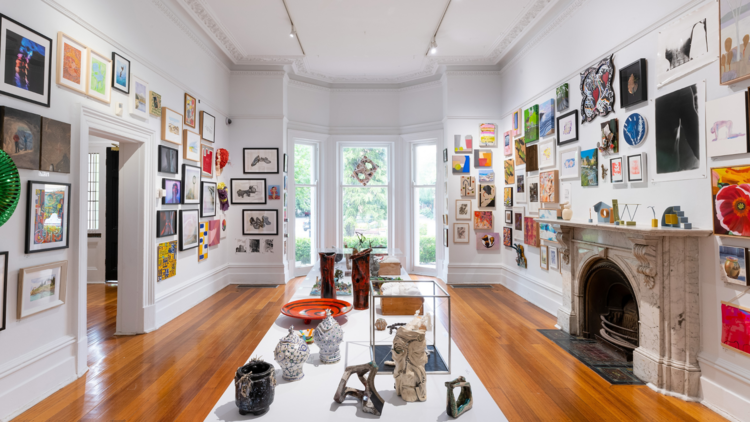 A room with walls covered in small artworks, a fireplace and a table in the centre holding small sculptures.