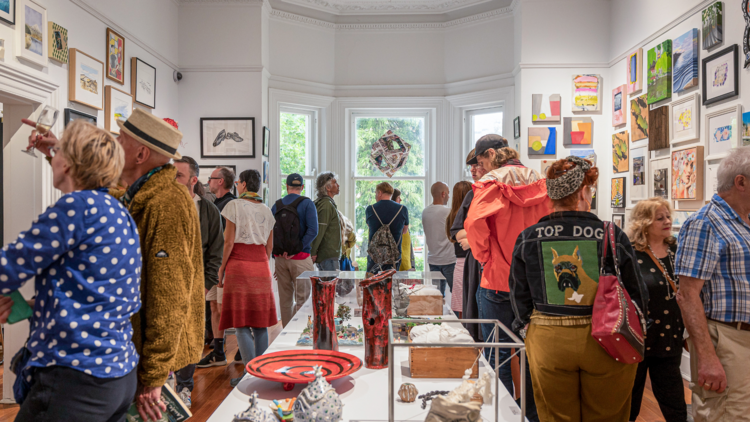 A  colourfully dressed crowd of people look at small artworks