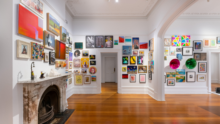 Small sculptures in front of a wall packed with small artworks