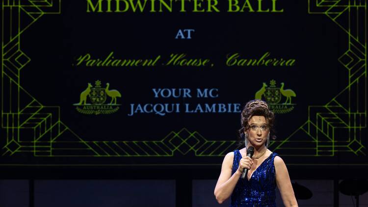 An actor playing Jacqui Lambie, with a sign in background saying: Midwinter Ball