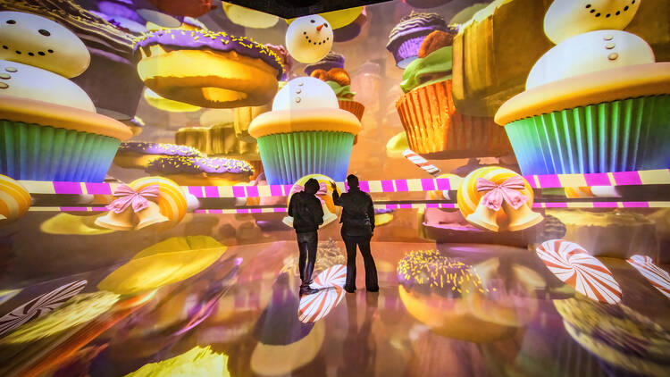 People stand inside ARTECHOUSE looking at digital images of cupcakes.