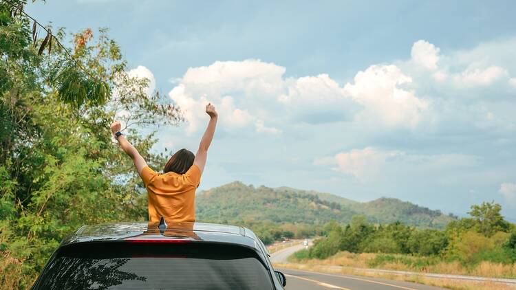 Female traveler in car throwing hands in the air 