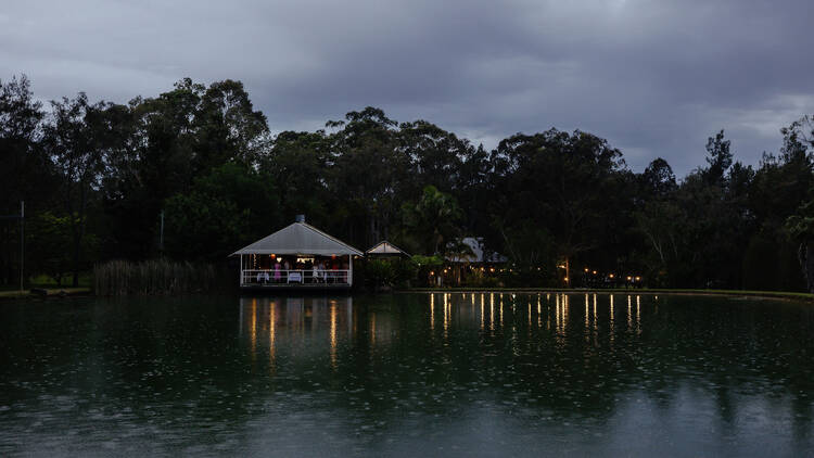 A restaurant with lights by a pond in the dark. 