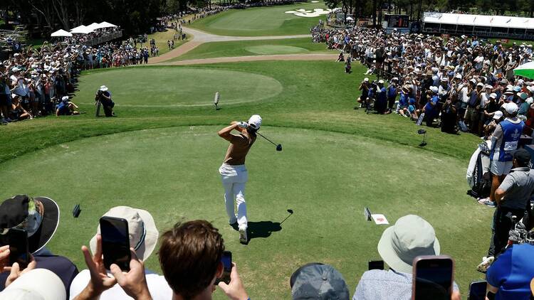 A golfer teeing off at the ISPS Handa Australian Open in front of a large crowd.