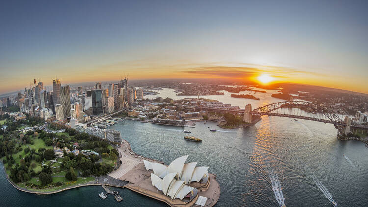 Sydney Harbour aerial at sunset with views of Royal Botanic Garden, the CBD, Sydney Opera House and Sydney Harbour Bridge.