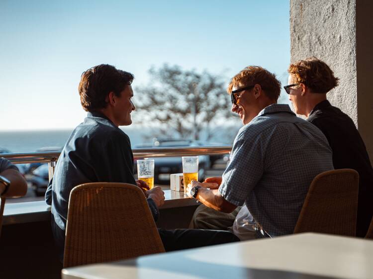 Three males drinking beers at window on balcony of pub