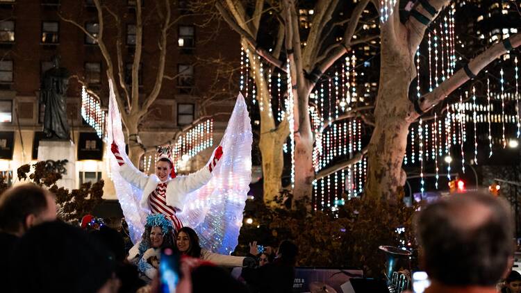 A dancer in an angel costume in front of an illuminated tree.