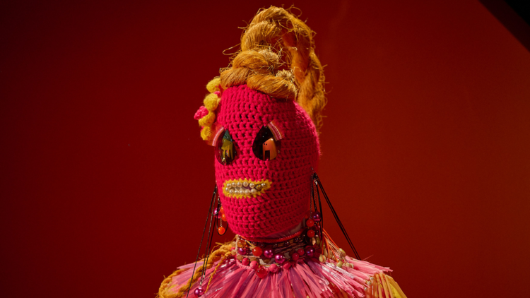 A red woven figure with a yellow mouth and ponytail